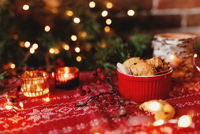 Red festive bowl full with christmas cookies, blurred christmas fir tree lights