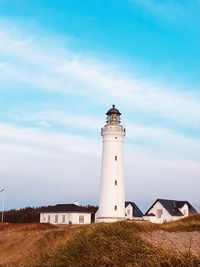 Lighthouse on field by building against sky