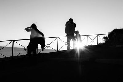 Silhouette men standing on railing against clear sky