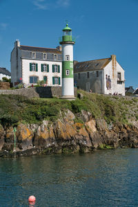 Lighthouse by sea against buildings