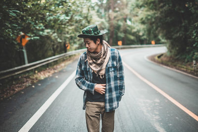 Portrait of young man standing on road against trees