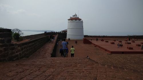 People on beach by lighthouse against sky