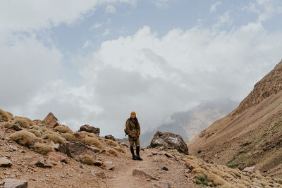 A women, standing with mustard color jacket with scenic view of rocks and mountains against sky