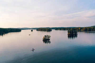 Aerial view of lakes, islands, forest and a person paddle boarding 