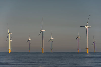 Wind turbines in sea against sky during sunset