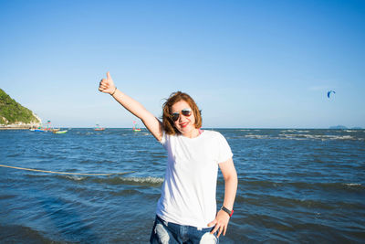 Portrait of smiling woman in sunglasses gesturing thumbs up sign against sea and sky