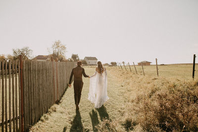 Friends standing on field by fence against clear sky