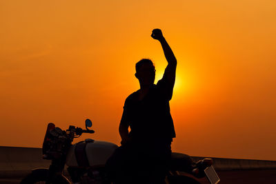 Silhouette man riding motorcycle against sky during sunset