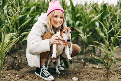 Happy girl with dog crouching at farm