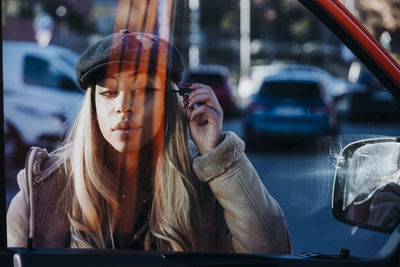 Ethnic female applying makeup near car