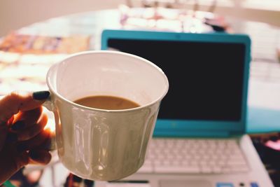 Cropped hand of woman holding coffee by laptop at home