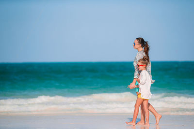 Side view of mother with daughter walking on beach