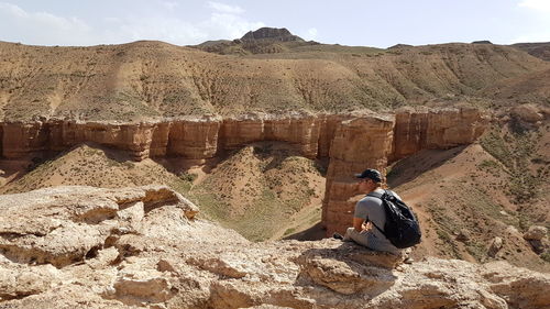 Rear view of man sitting on rock