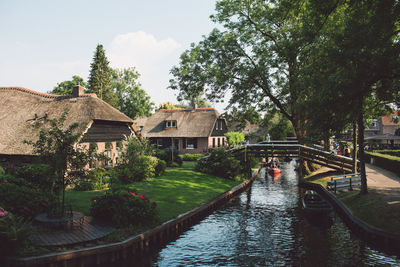 Canal amidst houses and trees against sky