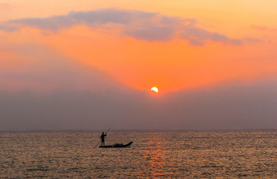 Silhouette person in sea against sky during sunset