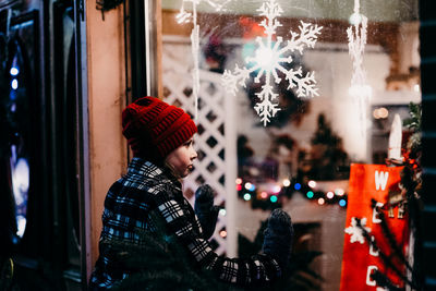 Girl looking at christmas decorations through glass at night