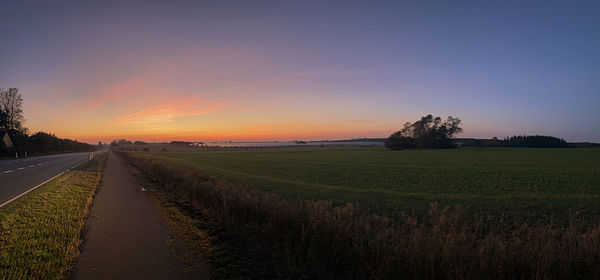 Empty road amidst field against sky during sunset