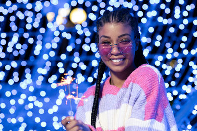 Cheerful black woman with braided hairstyle and pink glasses enjoying christmas lights