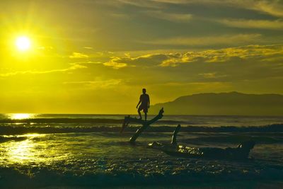 Silhouette man standing in sea against sky during sunset