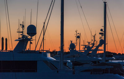 Sailboats moored in harbor at sunset