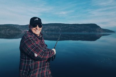 Portrait of happy man fishing at lake against sky