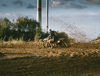 Man riding motorcycle on dirt road against sky