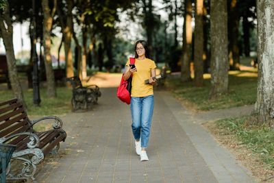 Portrait of a young student girl walking through the park with a backpack, a book 
