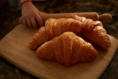 Child holding a rolling pin and croissants on a table.