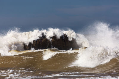 Waves splashing on shore against sky