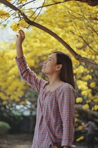 Young woman looking away while standing on tree