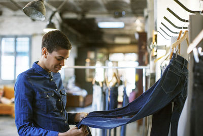 Smiling fashion designer checking jeans hanging on rack at workshop