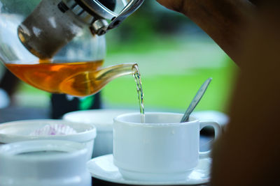 Cropped hand pouring tea in cup on table