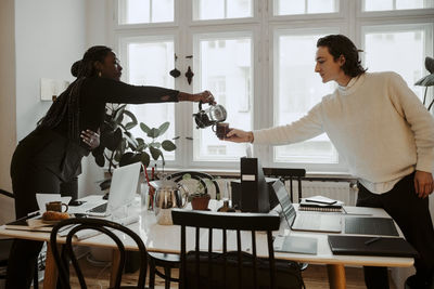 Female professional pouring coffee for male colleague in home office