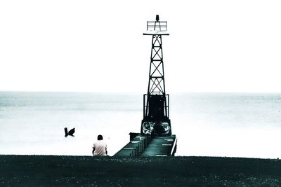 Man sitting on lighthouse by sea against clear sky