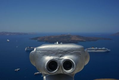 Close-up of coin-operated binoculars on sea against clear blue sky