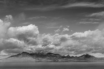 Scenic view of mountain range by lake against cloudy sky