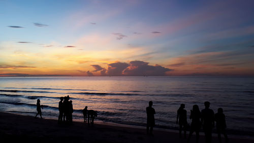 Silhouette people on beach against sky during sunset