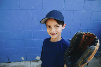 Portrait of happy boy wearing baseball glove standing against wall