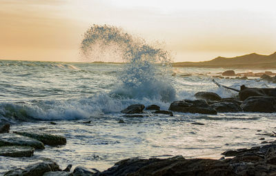 Waves splashing on rocks at shore against sky