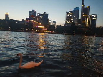 Illuminated buildings by river against sky in city