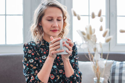 Thoughtful woman with mug sitting on sofa at home