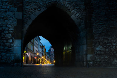 Illuminated street seen through archway in city at night