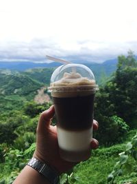 Close-up of hand holding drink against landscape