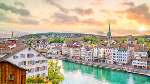 High angle view of buildings by river against cloudy sky