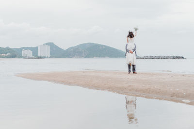 Newlywed couple standing on beach against sky