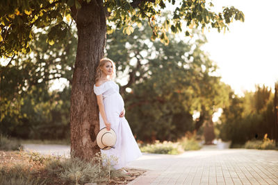 Pregnant woman leaning on tree at park