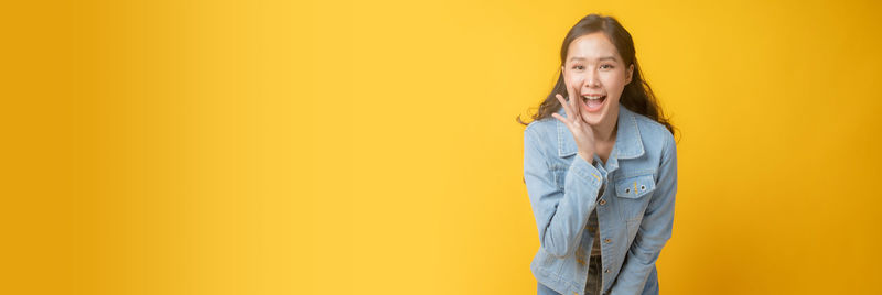 Portrait of smiling young woman against yellow background