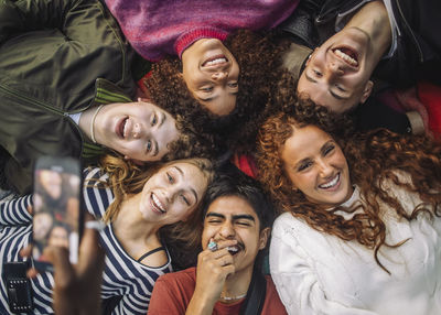 Hand of unrecognizable person photographing cheerful teenage friends having fun while lying down at park