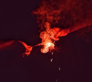 Close-up of hand with bonfire against sky at night