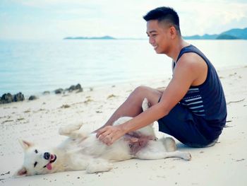 Man with dog sitting on beach against sky